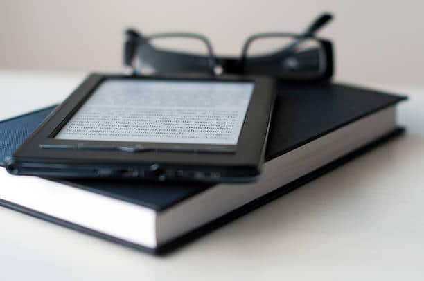 Liseuse électronique posée sur un livre papier avec une paire de lunettes de lecture